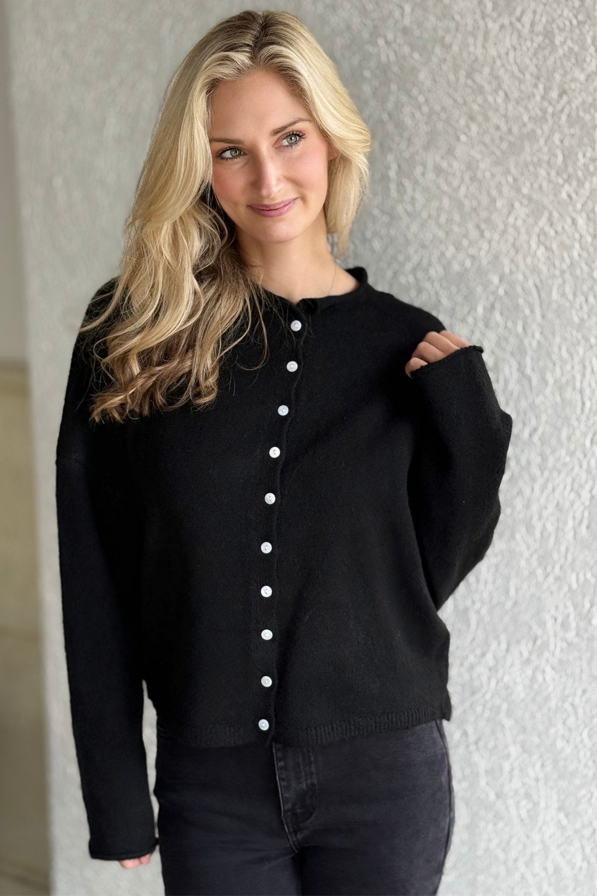 Woman wearing The Monroe Button Front Cardigan — black soft knit button-down cardigan with drop shoulders, ribbed cuffs, and a crew neckline.