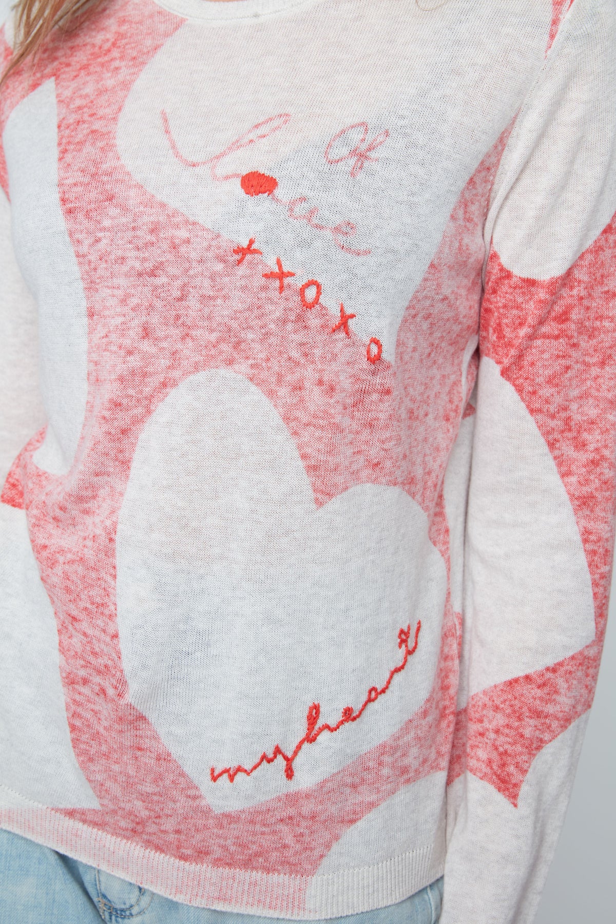Close-up of a sweater with heart designs and red text on a white background