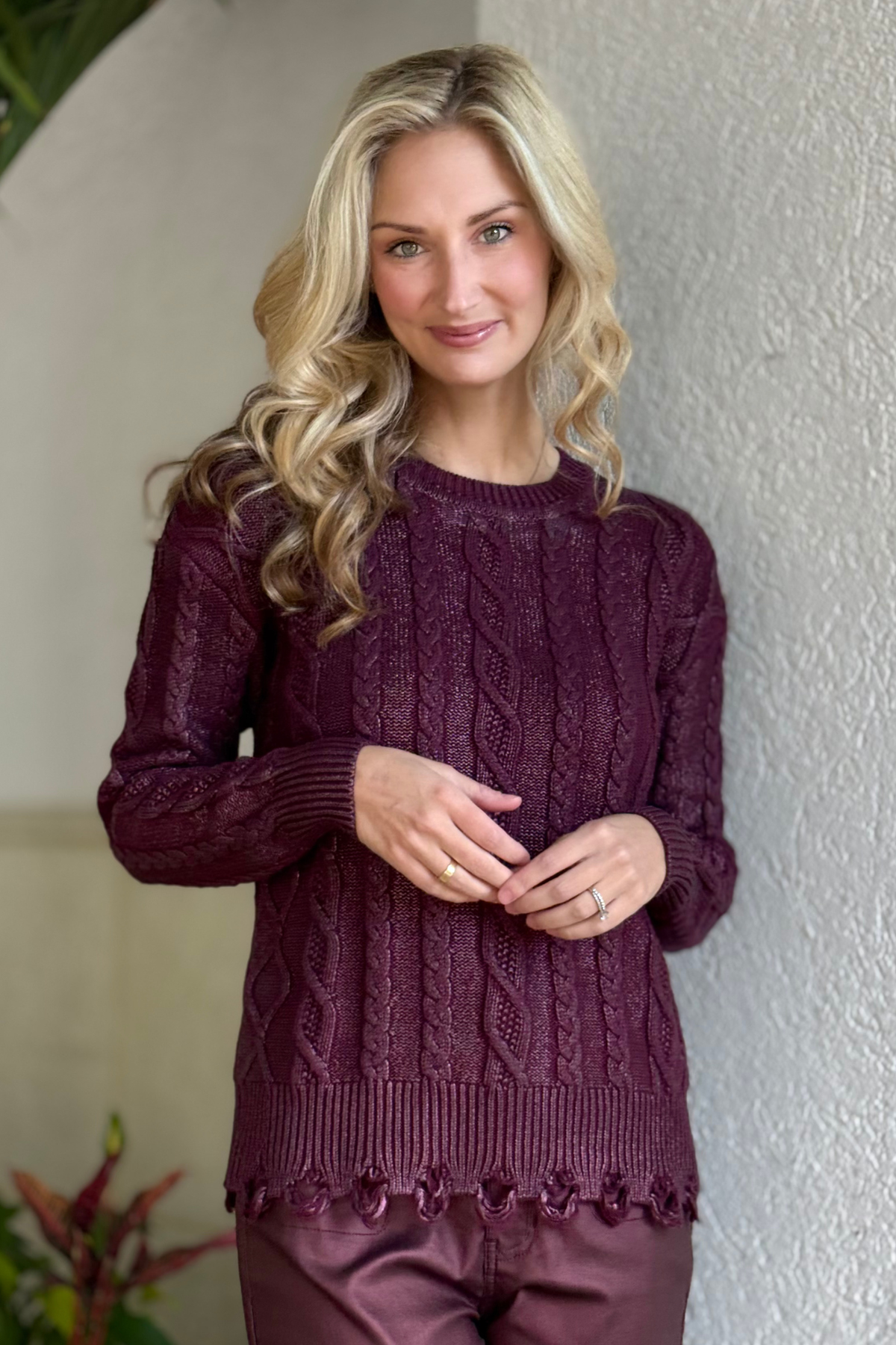 Woman wearing Charlie B Metallic Cable Knit Sweater in Cabernet with metallic sheen and distressed hem.