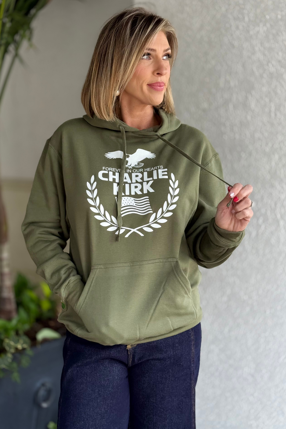 Woman wearing olive Charlie Kirk Forever in Our Hearts hoodie