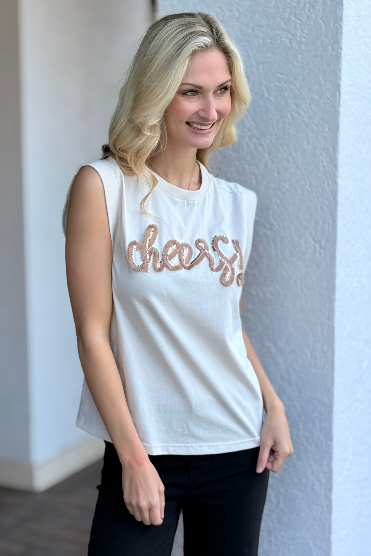 Model wearing ivory sleeveless top with sequin embroidered “cheers” design