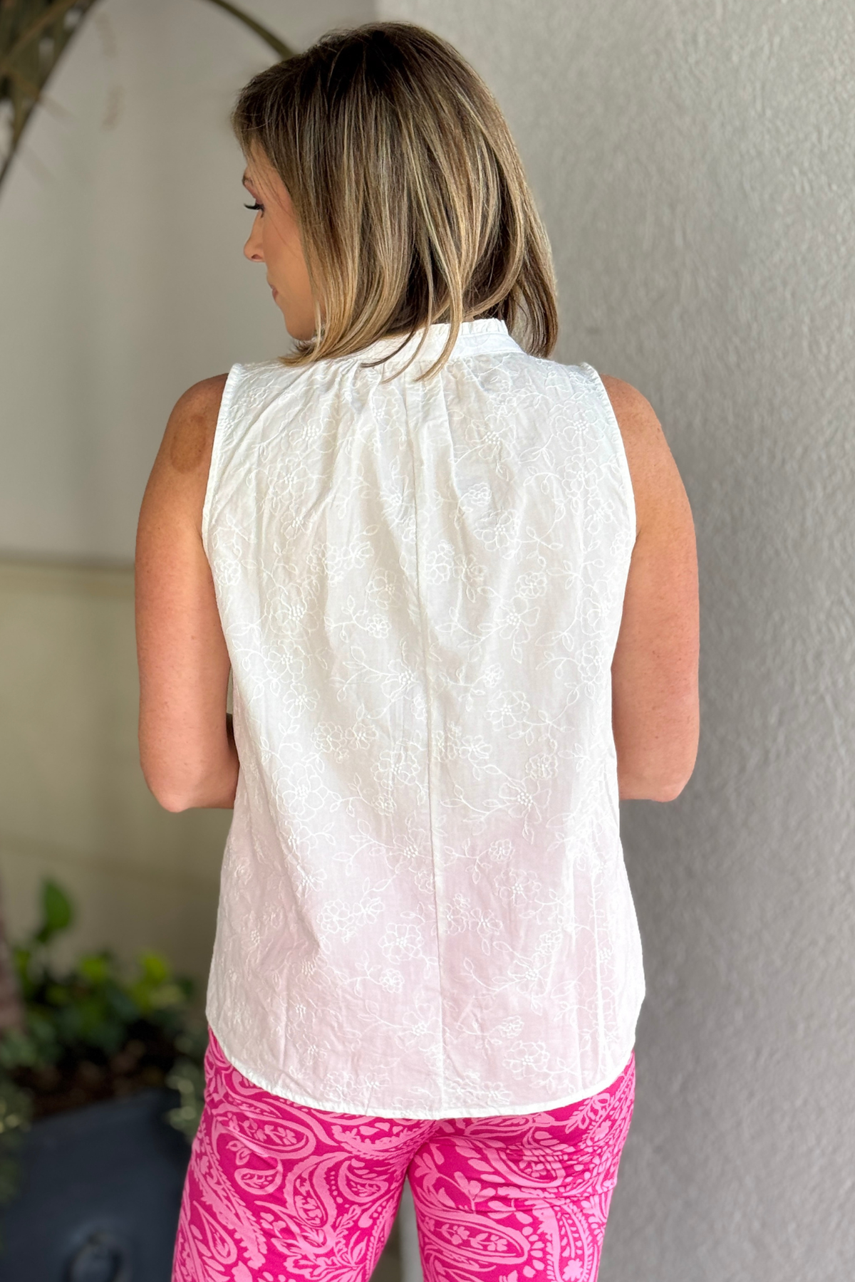 Woman wearing TPN Camellia sleeveless white blouse paired with printed pink pants