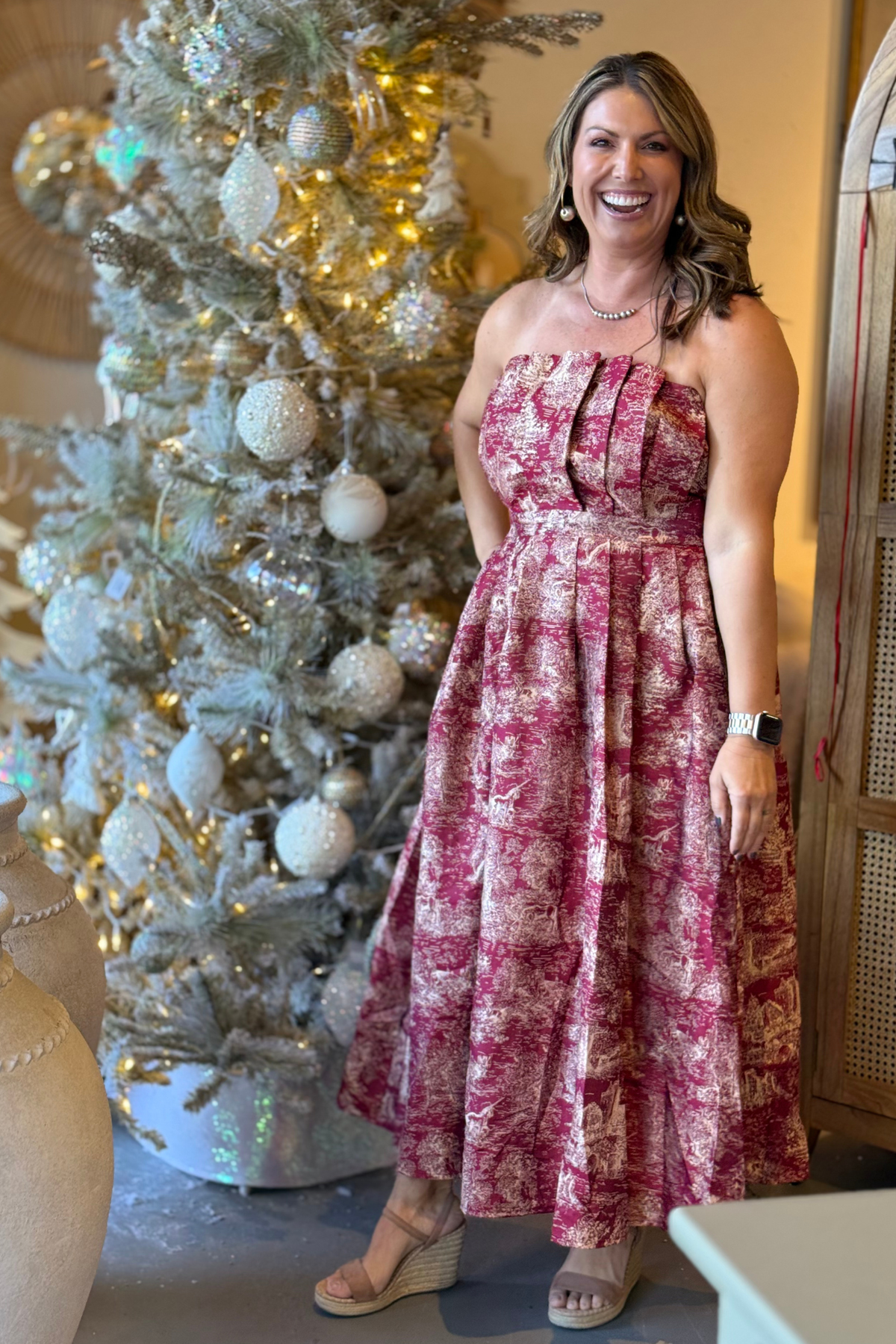 Woman wearing burgundy Toile Jacquard Strapless Midi Dress in front of Christmas tree.