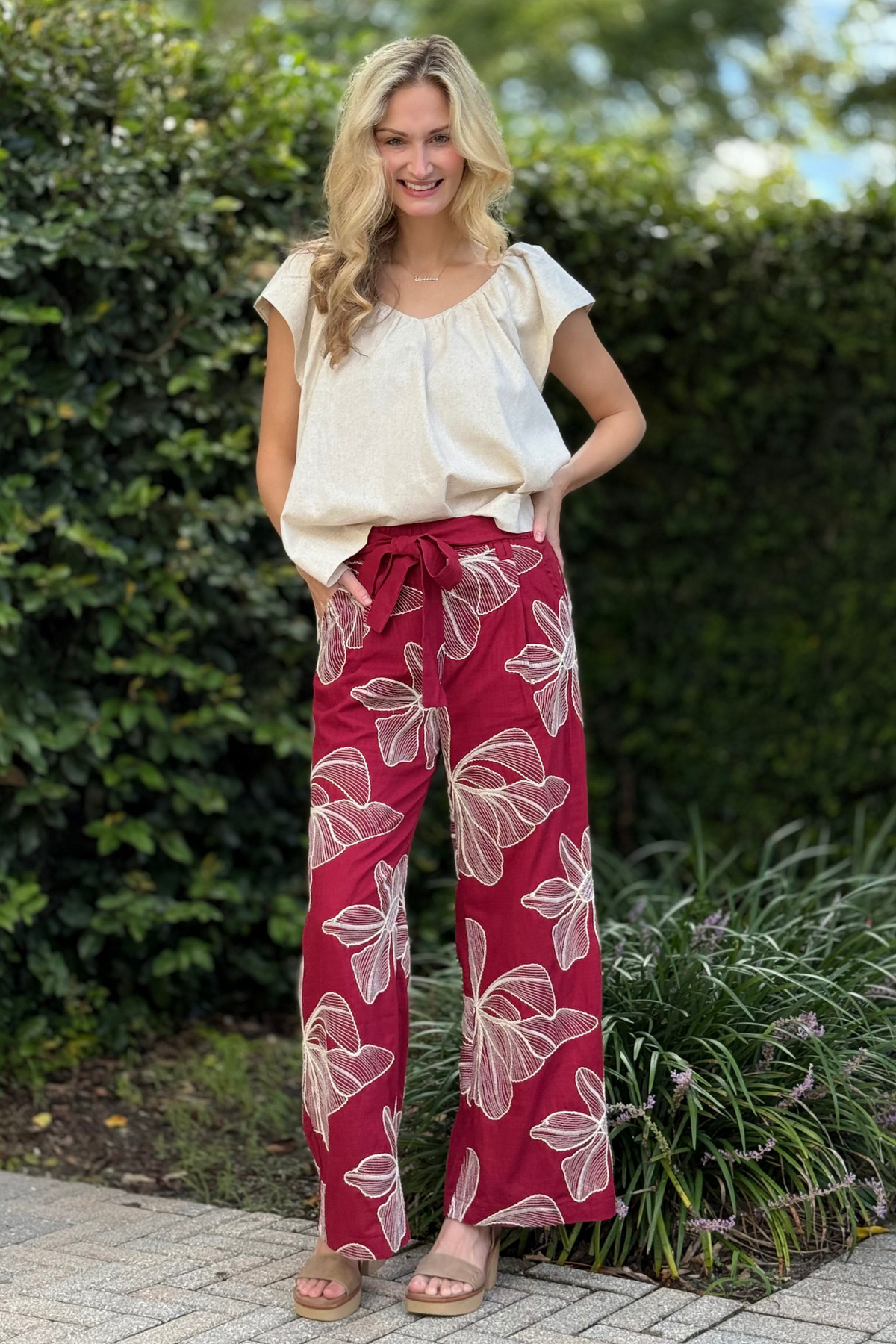Woman wearing Vineyard Petal Pants in burgundy with oversized floral embroidery, elastic tie waist, and shorts lining.