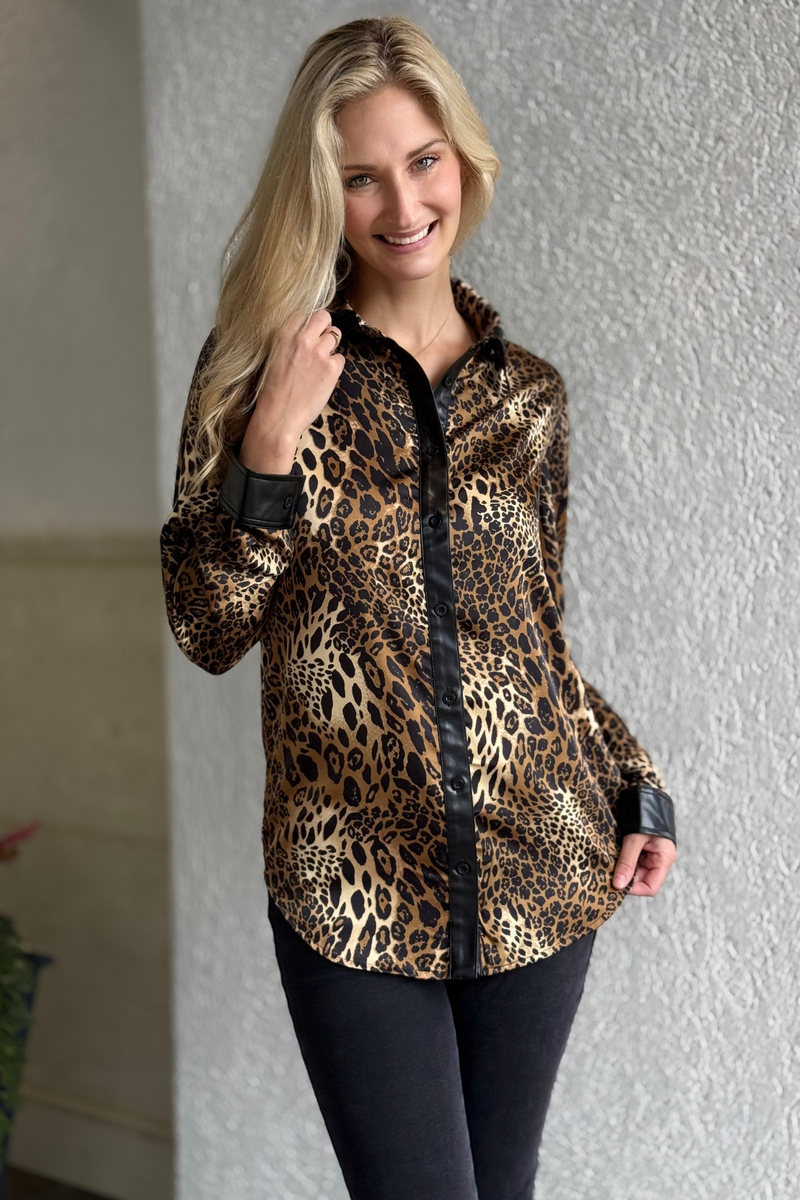 Model wearing the Frank Lyman Luxe Safari Blouse — silky leopard print button-down top with faux leather trim on collar, cuffs, and placket.