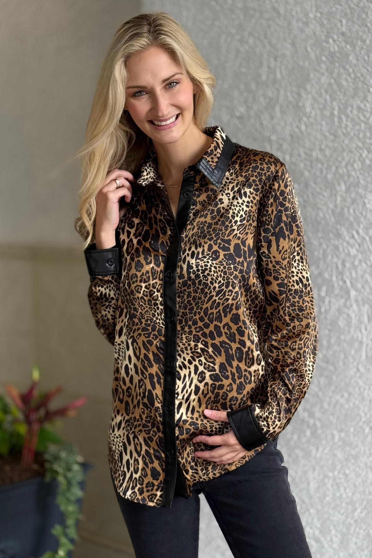 Model wearing the Frank Lyman Luxe Safari Blouse — silky leopard print button-down top with faux leather trim on collar, cuffs, and placket.