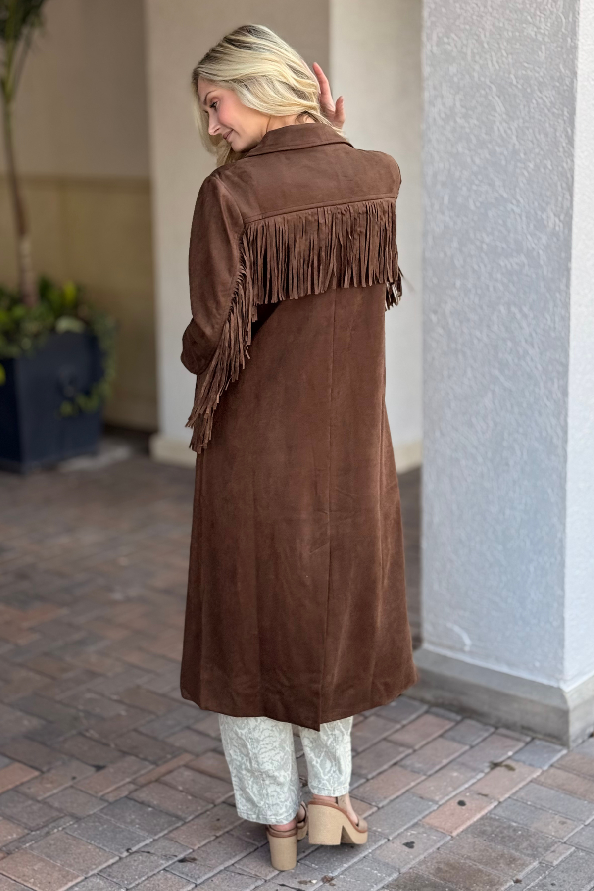 Woman wearing a brown suede coat with fringe, standing on a patio.