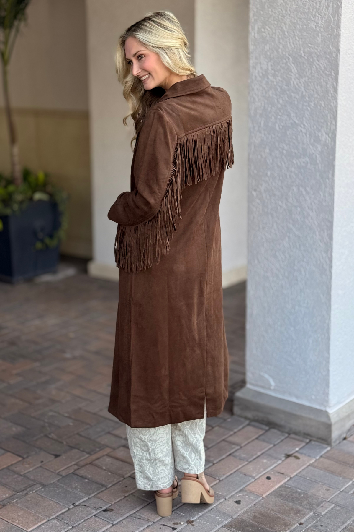 Woman wearing a brown suede coat with fringe standing on a sidewalk.