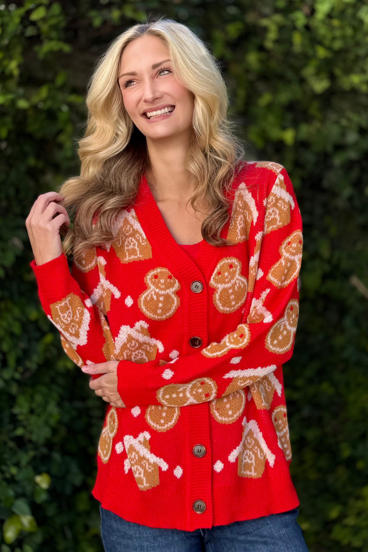 Woman wearing red holiday cardigan with gingerbread and snowman pattern from The Pink Nickel TPN Collection