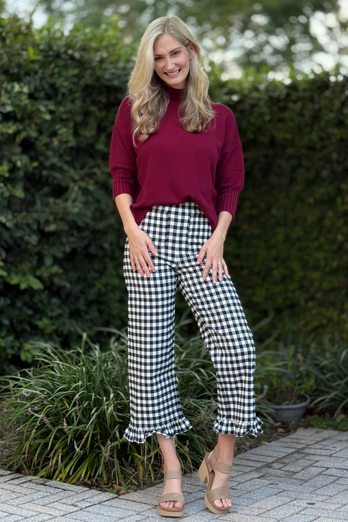 Lifestyle shot of gingham ruffle trim pants styled with a tucked-in blouse and heels
