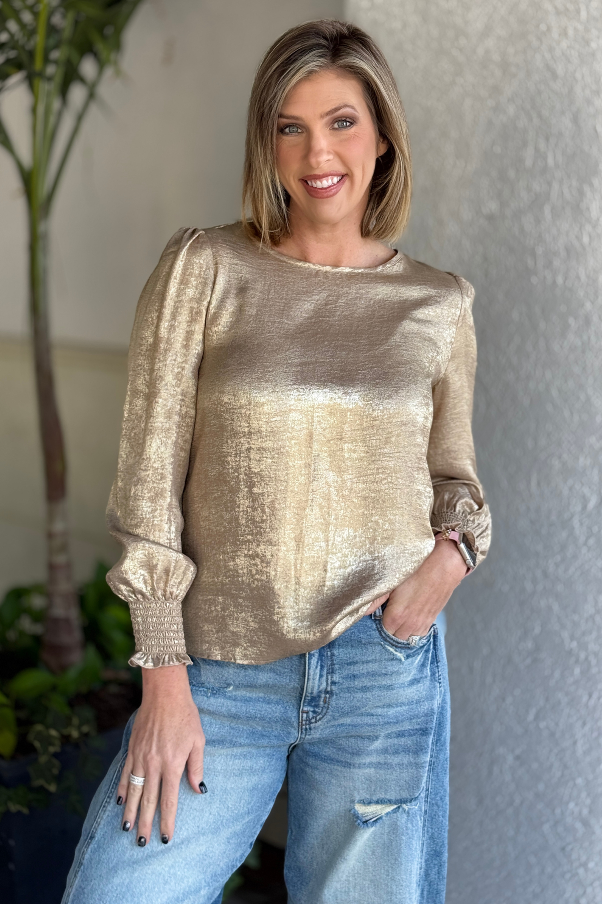 Woman wearing gold metallic smocked long sleeve blouse with jeans