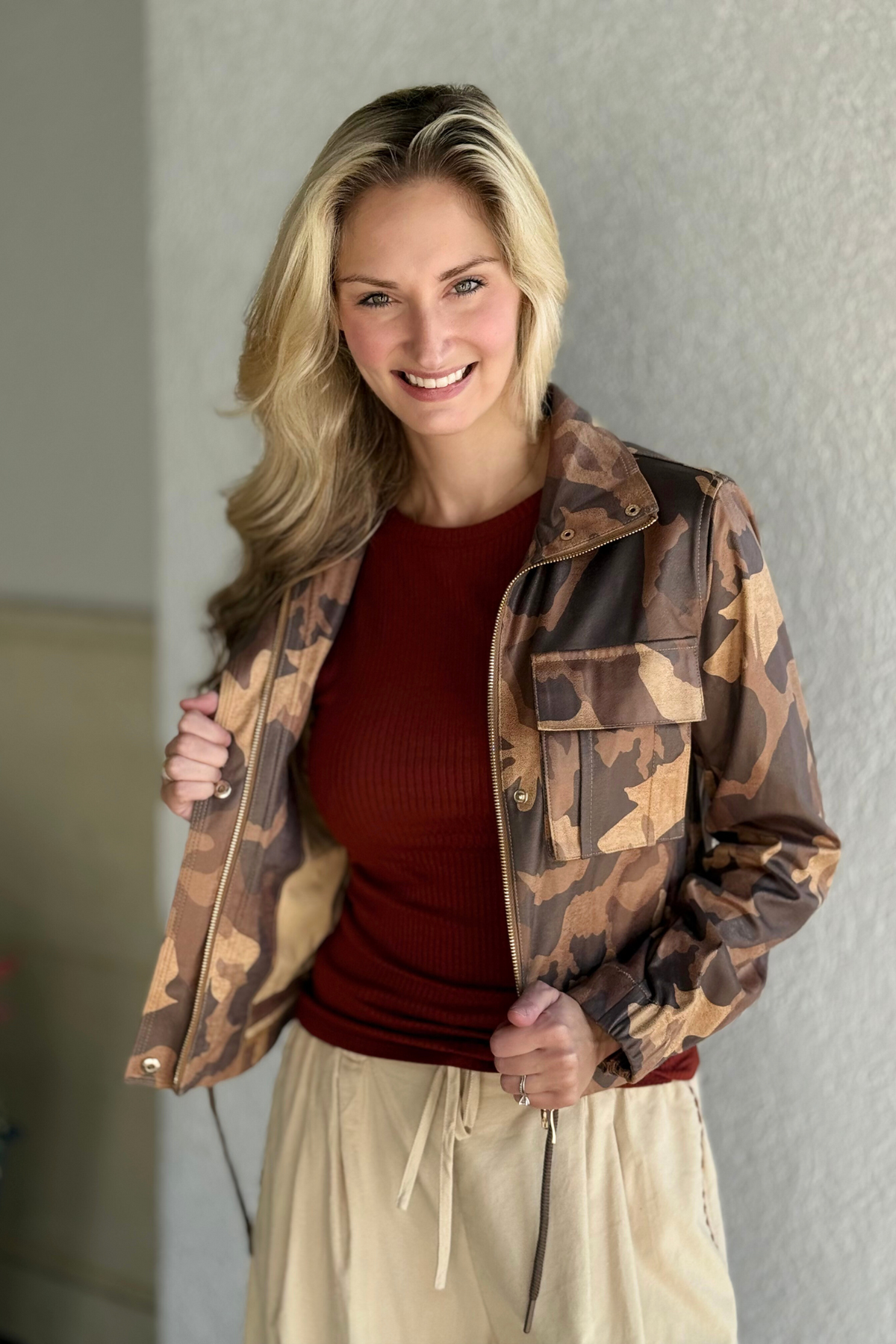 Woman wearing the Insight Jacket in brown camo vegan leather with zipper details and drawstring hem, styled with a rust ribbed top and cream pants.