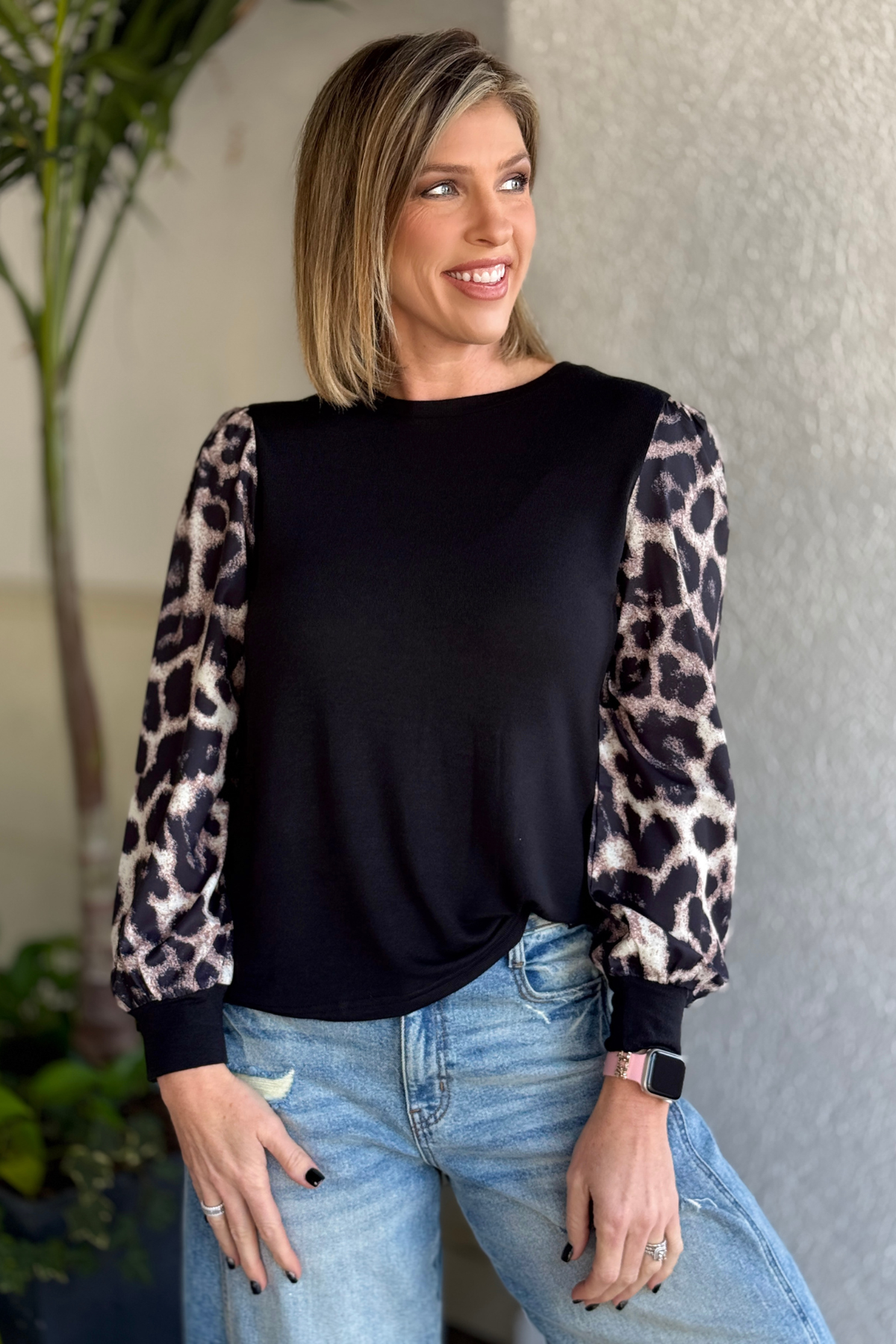 Woman wearing black leopard puff sleeve top styled with denim jeans