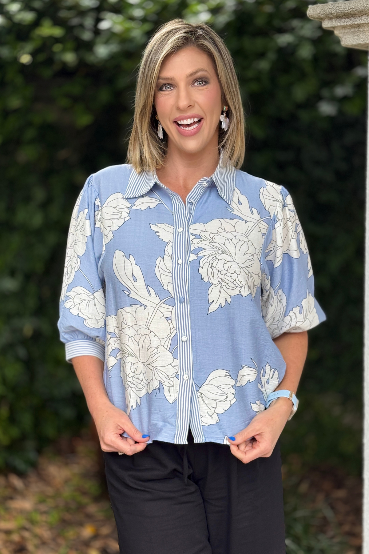 Model wearing misty blue floral button down top with black pants