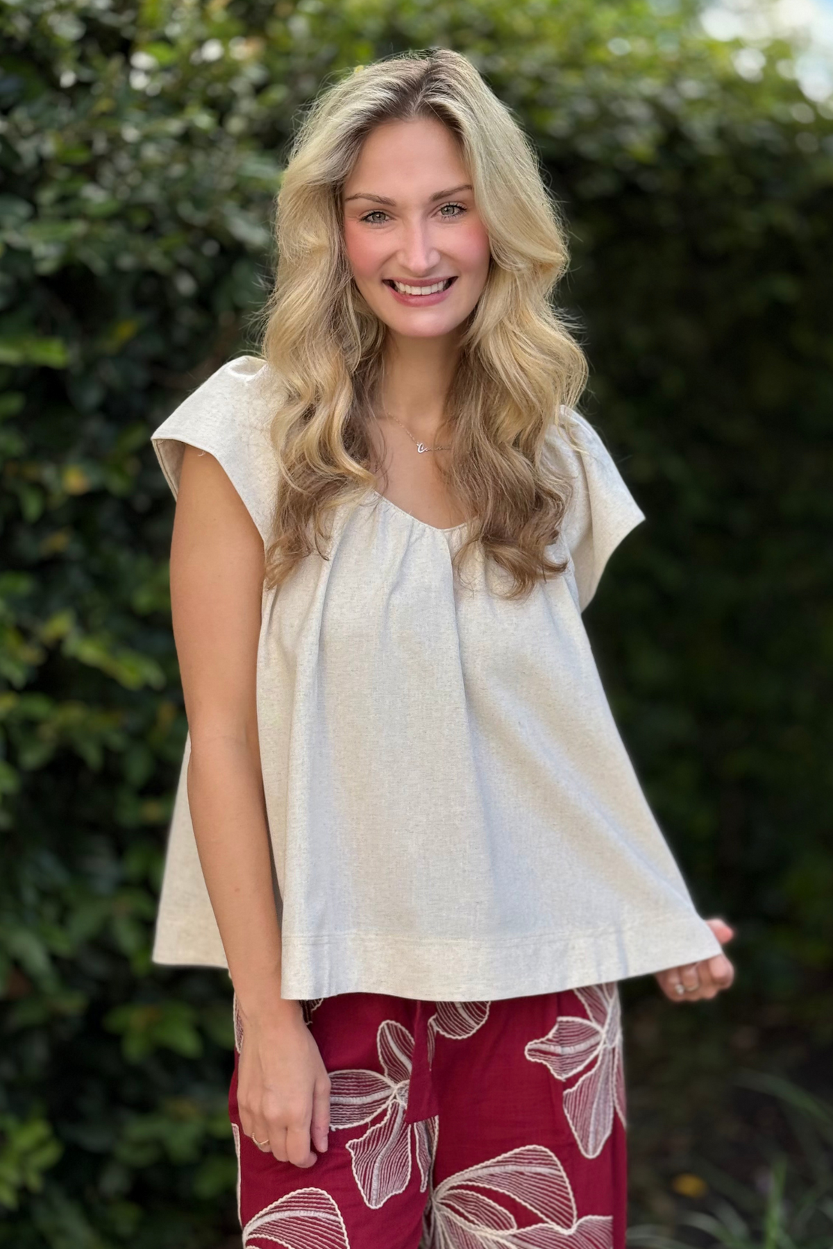Woman wearing an oatmeal linen V-neck top with padded cap sleeves and a relaxed fit.