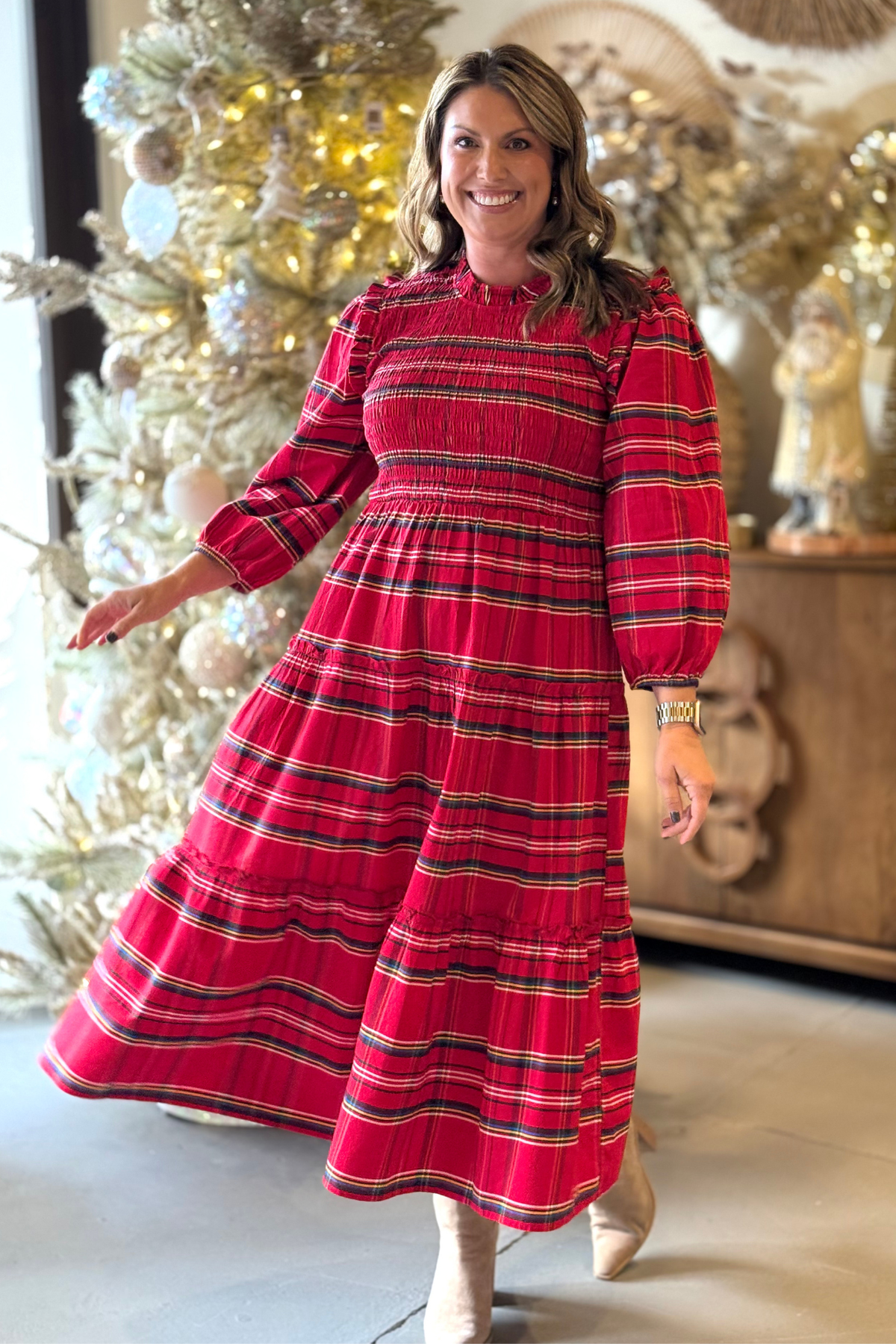 Woman wearing red plaid Mud Pie midi dress with smocked bodice and long sleeves, styled with neutral ankle boots.
