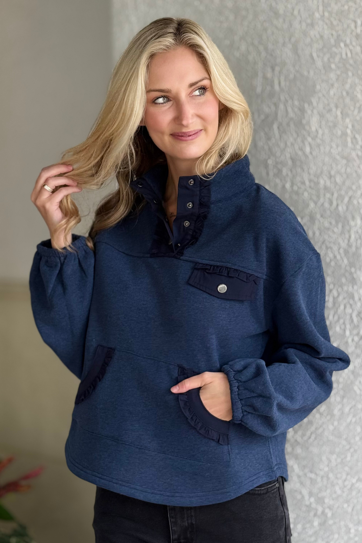 Woman wearing navy ruffle trim quarter snap sweatshirt with kangaroo pocket and puff sleeves.