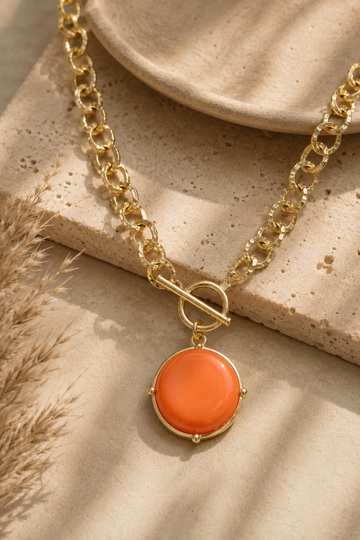 Gold toggle necklace with orange stone pendant.