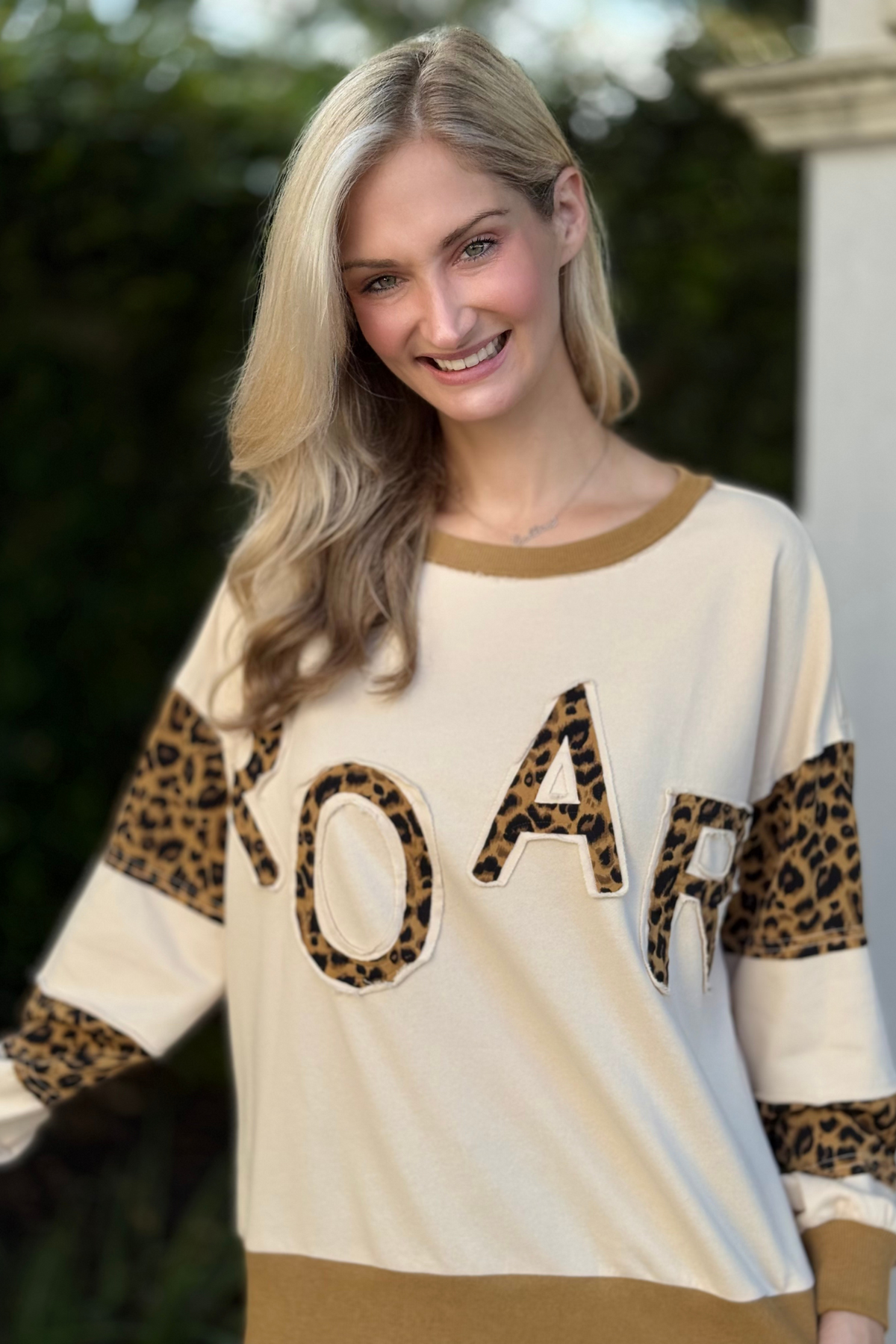 Close-up of leopard “ROAR” appliqué lettering on cream sweatshirt
