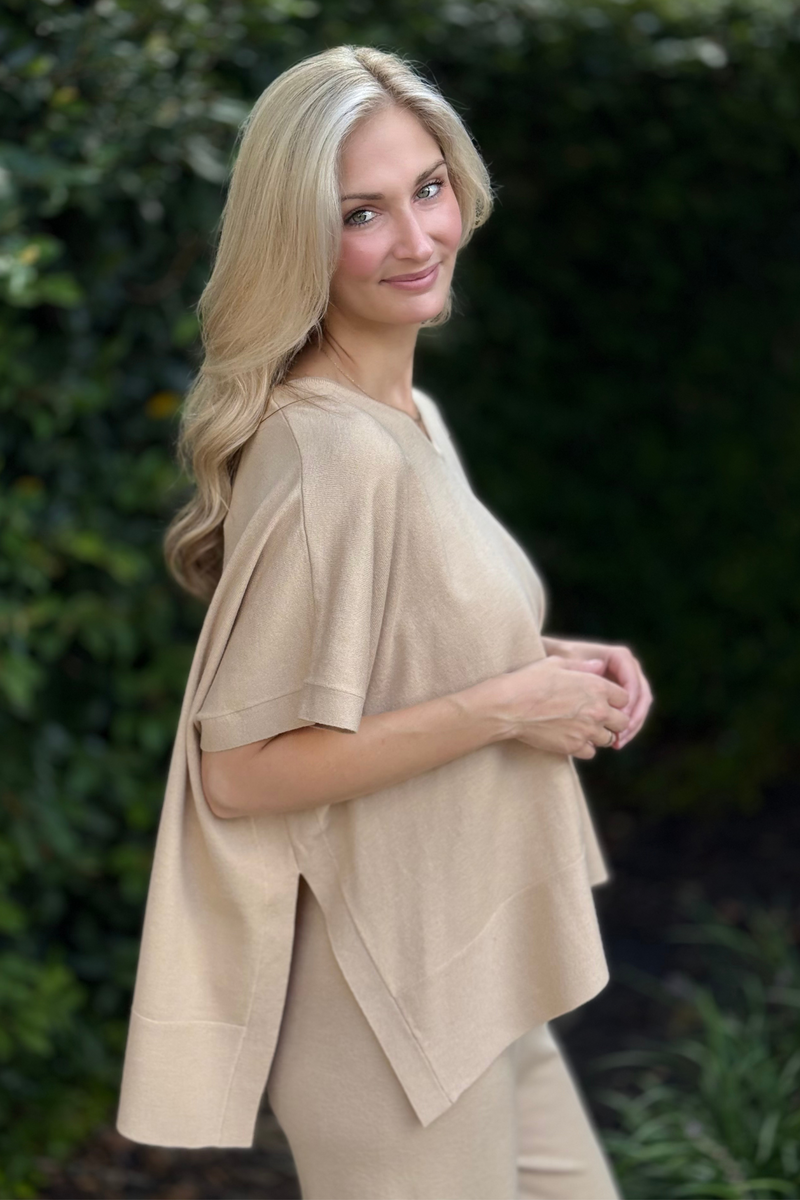 Side view showing the draped poncho silhouette and relaxed fit in tan knit