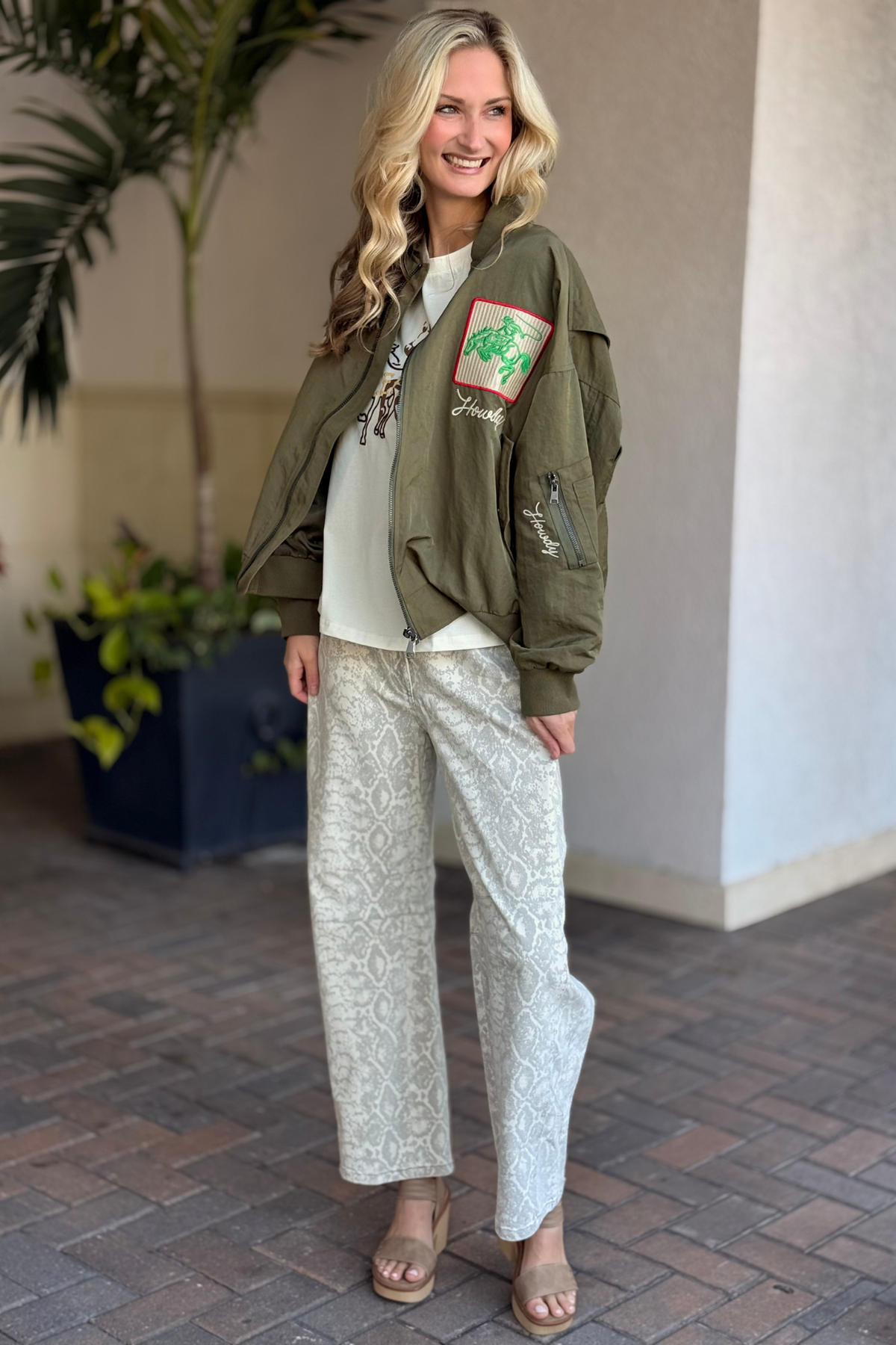 Model wearing olive embroidered rodeo bomber jacket layered over graphic tee