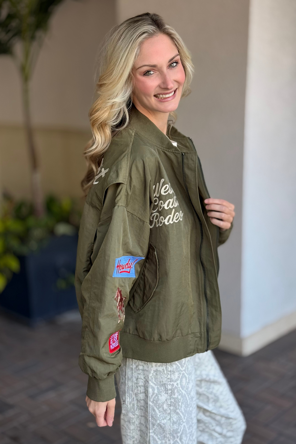 Side view of olive bomber jacket featuring zippered sleeve pocket and patches