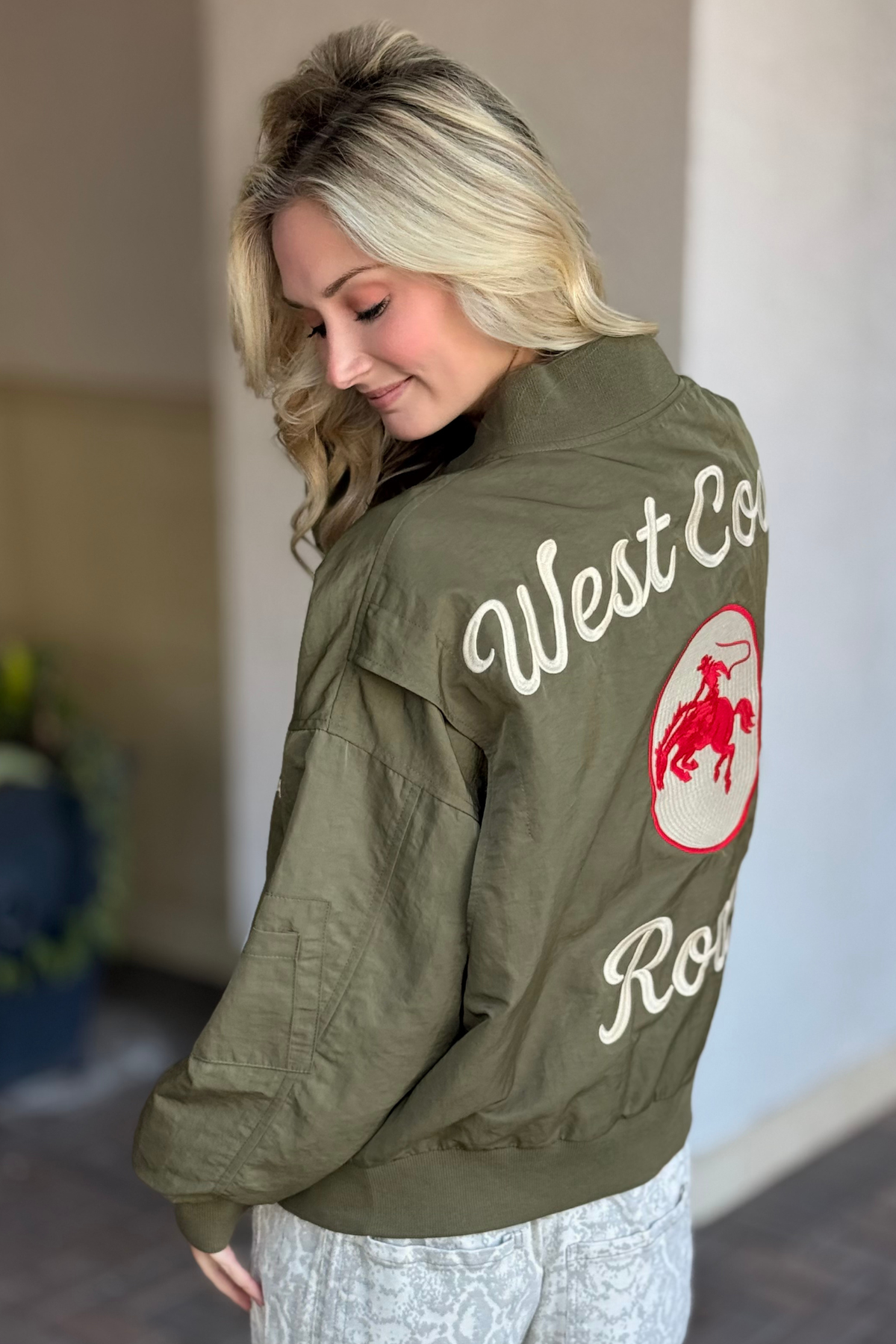 Woman wearing a green jacket with 'West Coast' and a logo on the back.