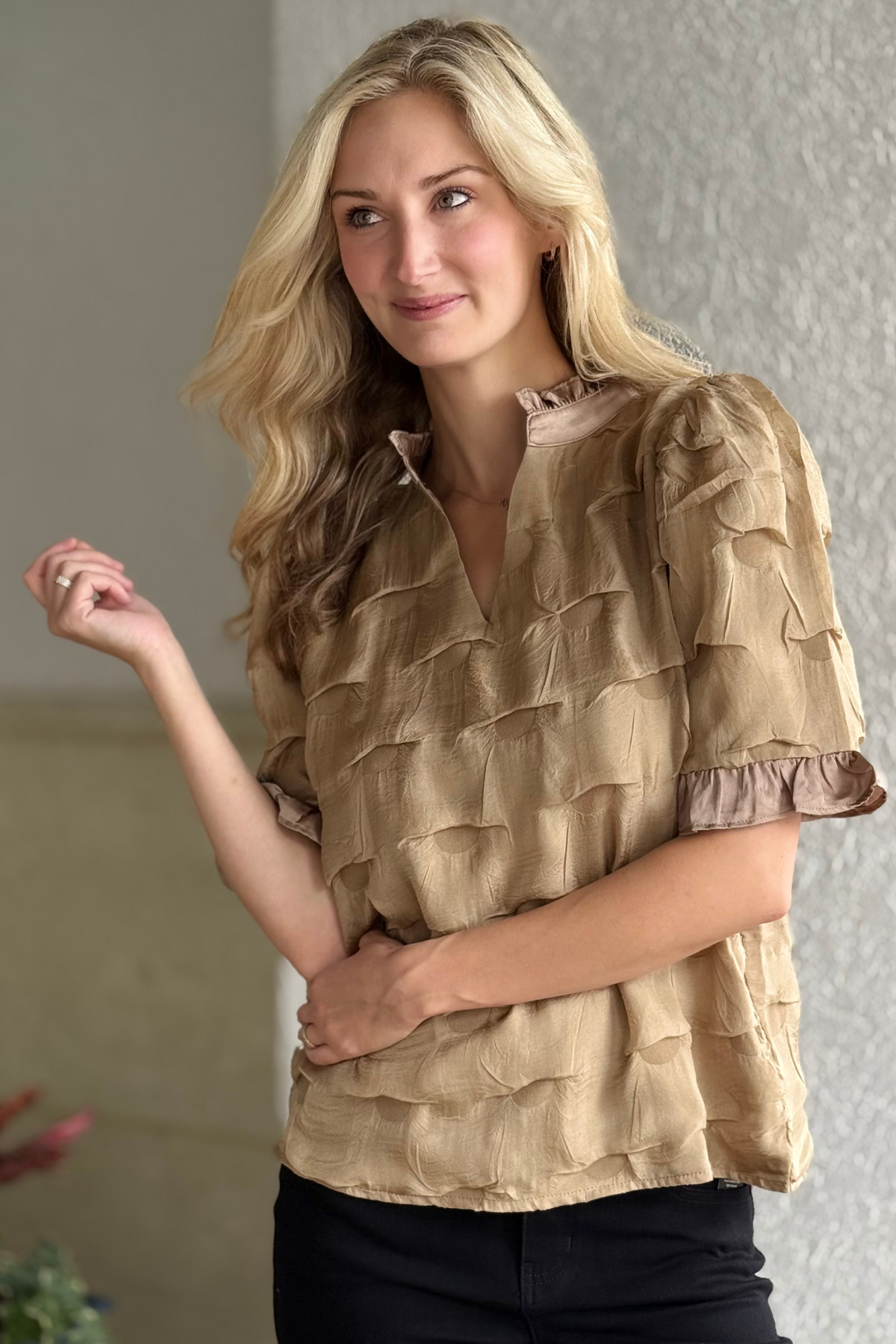 Woman wearing Satin Whisper Textured Ruffle Blouse in sand with ruffled details and tonal dot texture.