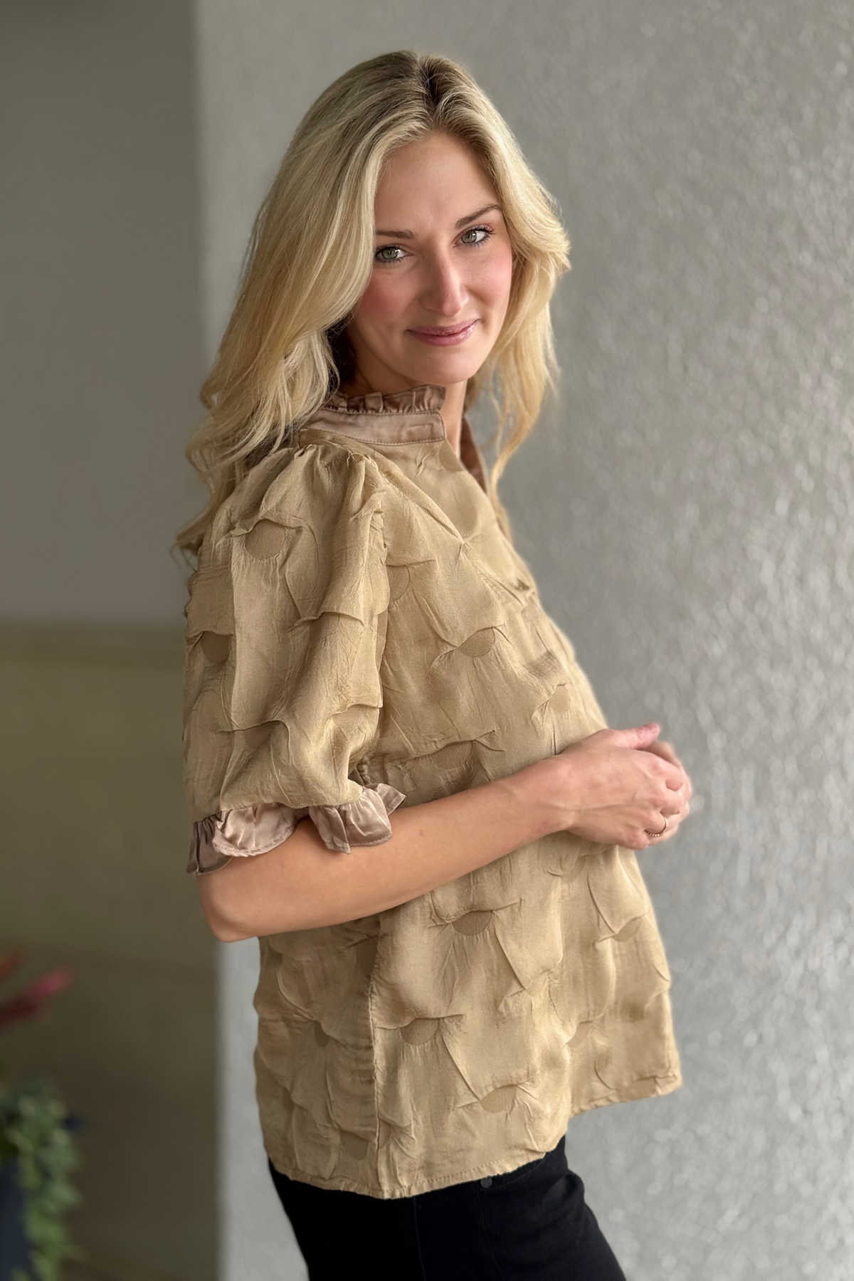 Woman wearing a beige layered blouse against a neutral background