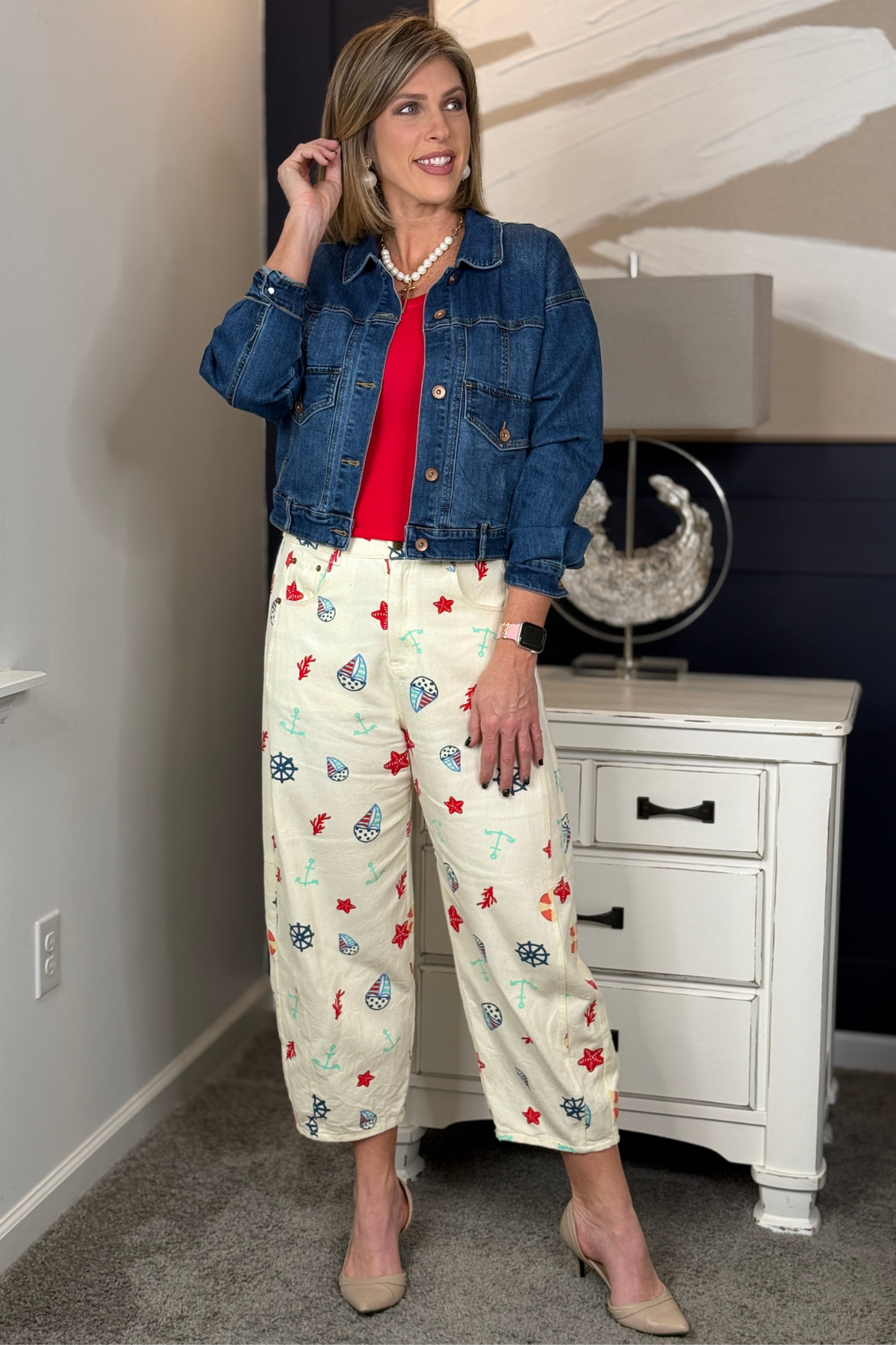Woman wearing marine inspired printed wide leg pants with anchors and nautical icons styled with a white crop tank for summer vacation outfit.