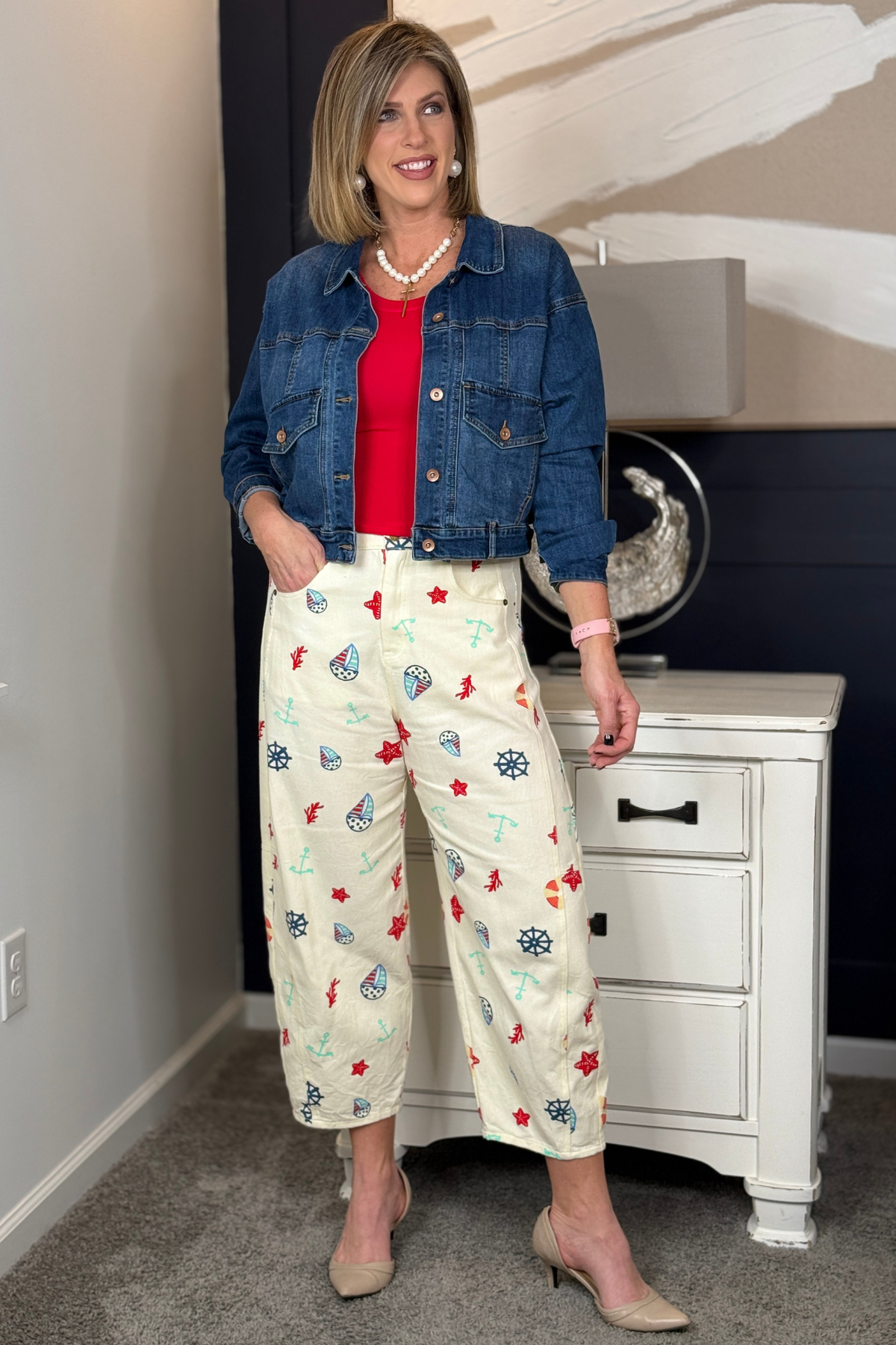 Woman wearing a denim jacket, red top, and patterned pants in a room.