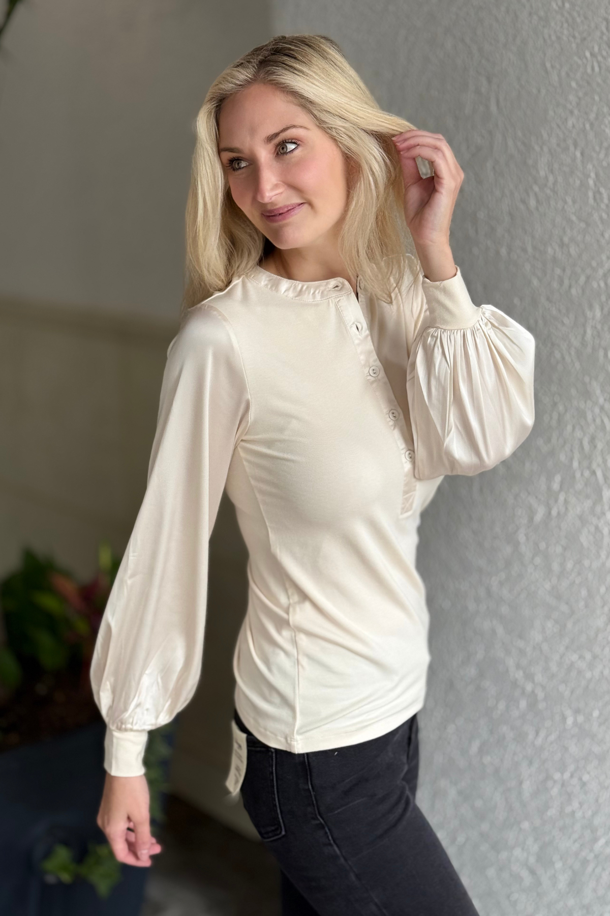 Woman wearing a cream-colored blouse with puffed sleeves against a neutral background