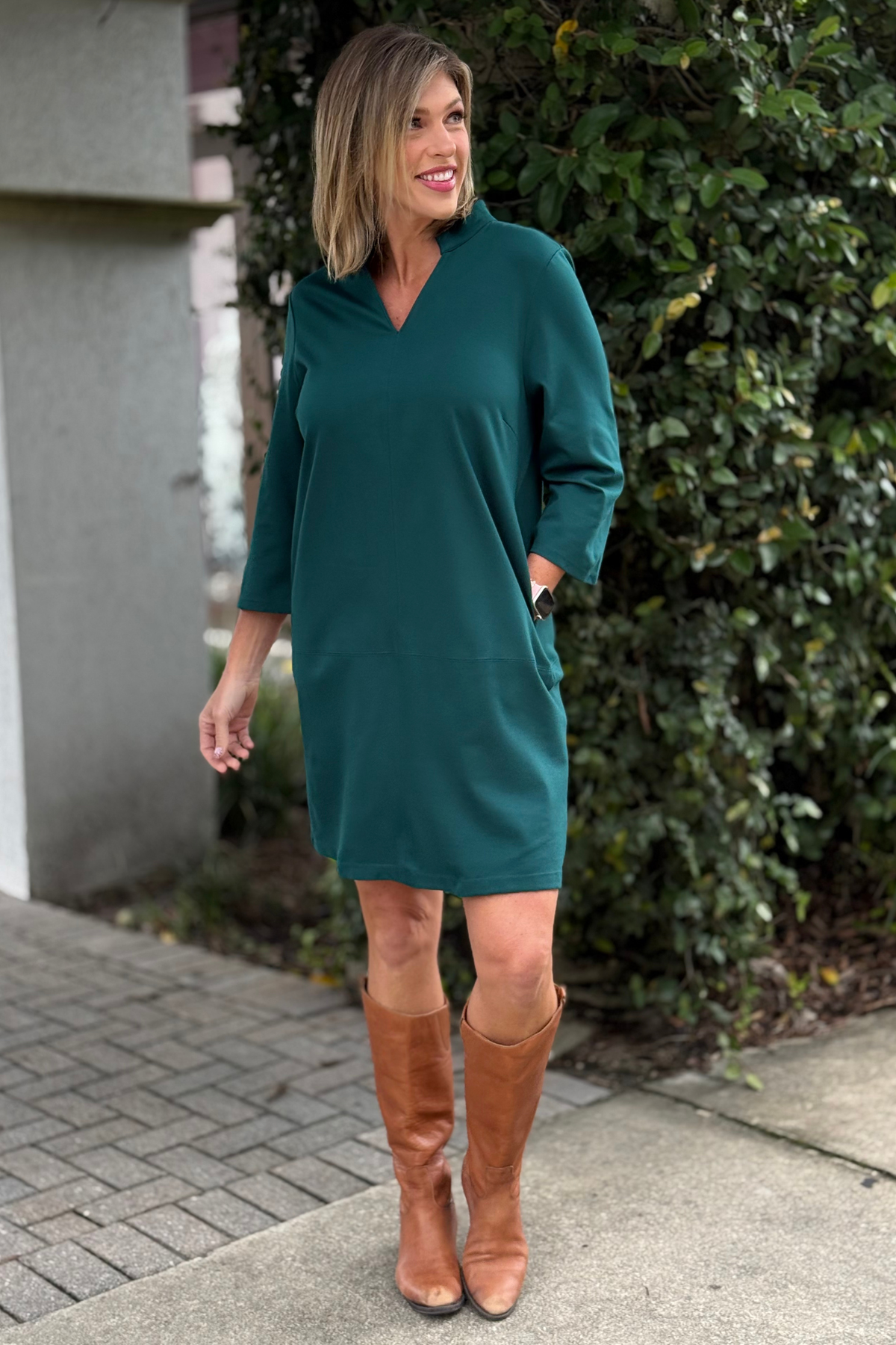 Woman wearing the TPN Portfolio Dress in hunter green with 3/4 sleeves, v-neckline, and side pockets.