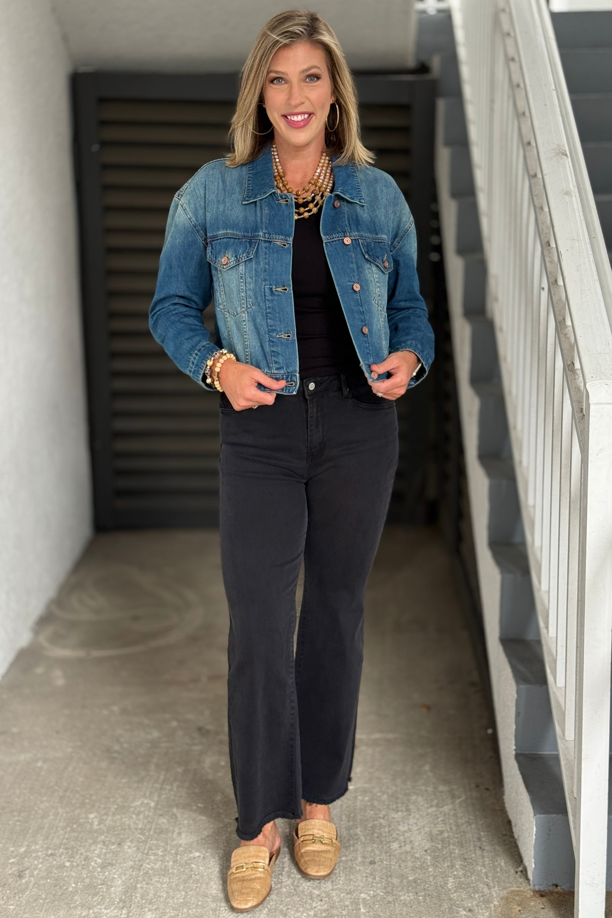 Woman wearing Tribal Fountain cropped denim jacket over a black tank and black jeans.