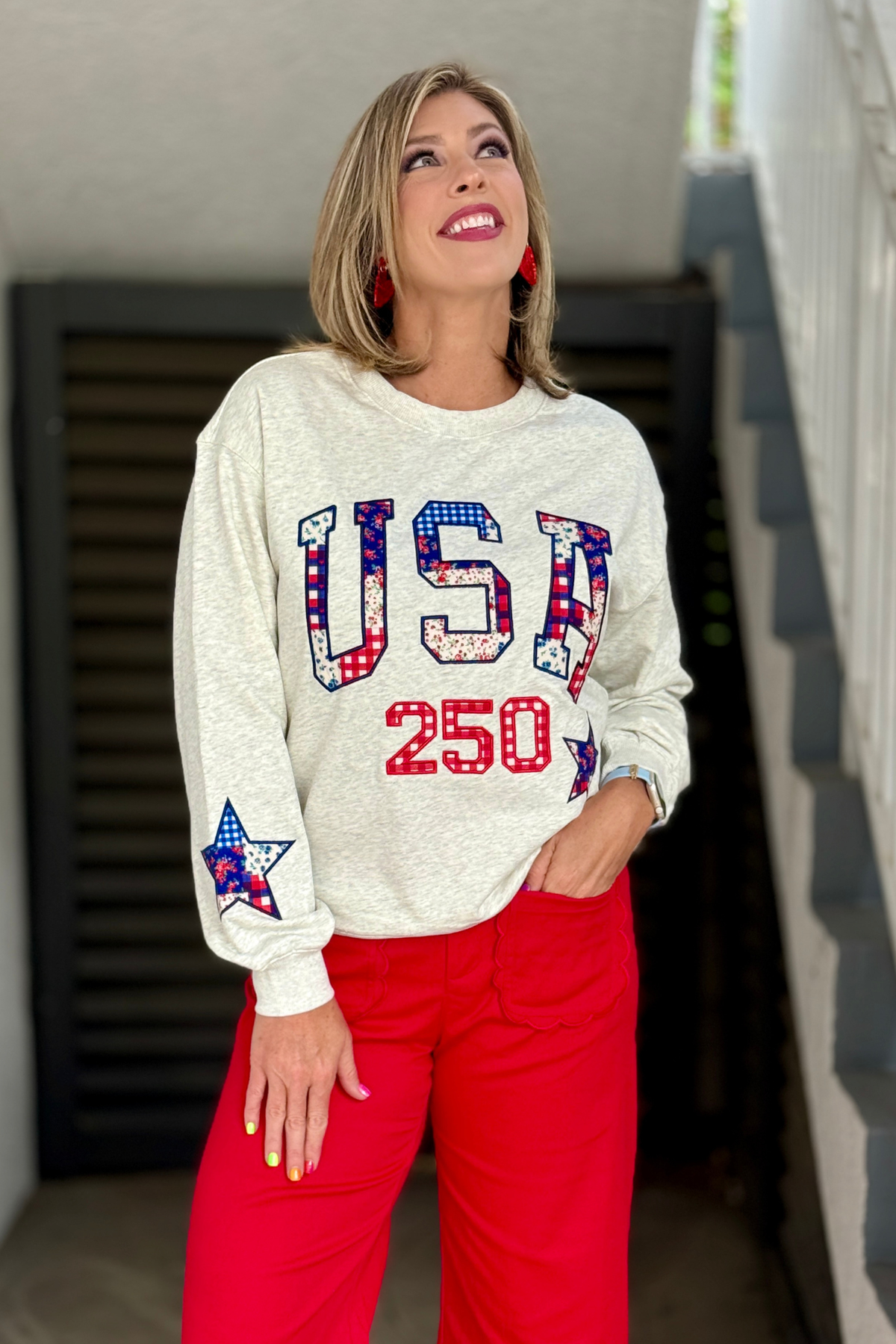 Woman wearing heather grey USA 250 patriotic sweatshirt with red scallop pants