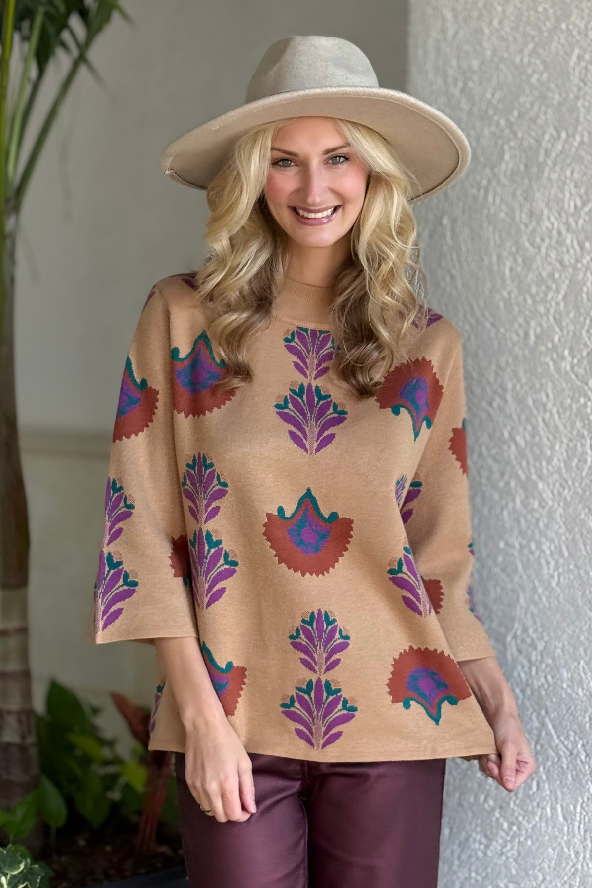 Woman wearing a camel floral knit sweater with purple, teal, and rust patterns and a relaxed fit.