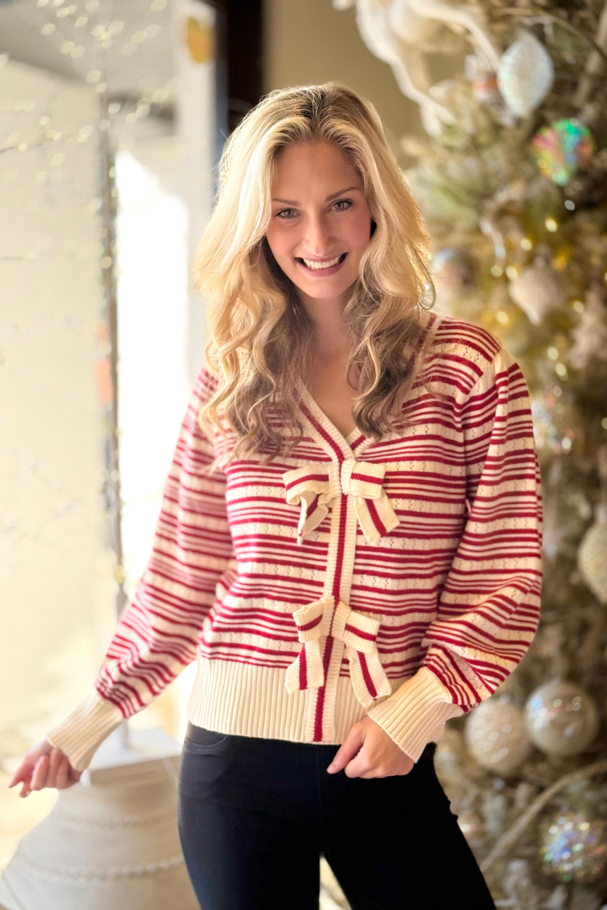 Woman wearing a red and cream striped V-neck sweater with bow details on the front.
