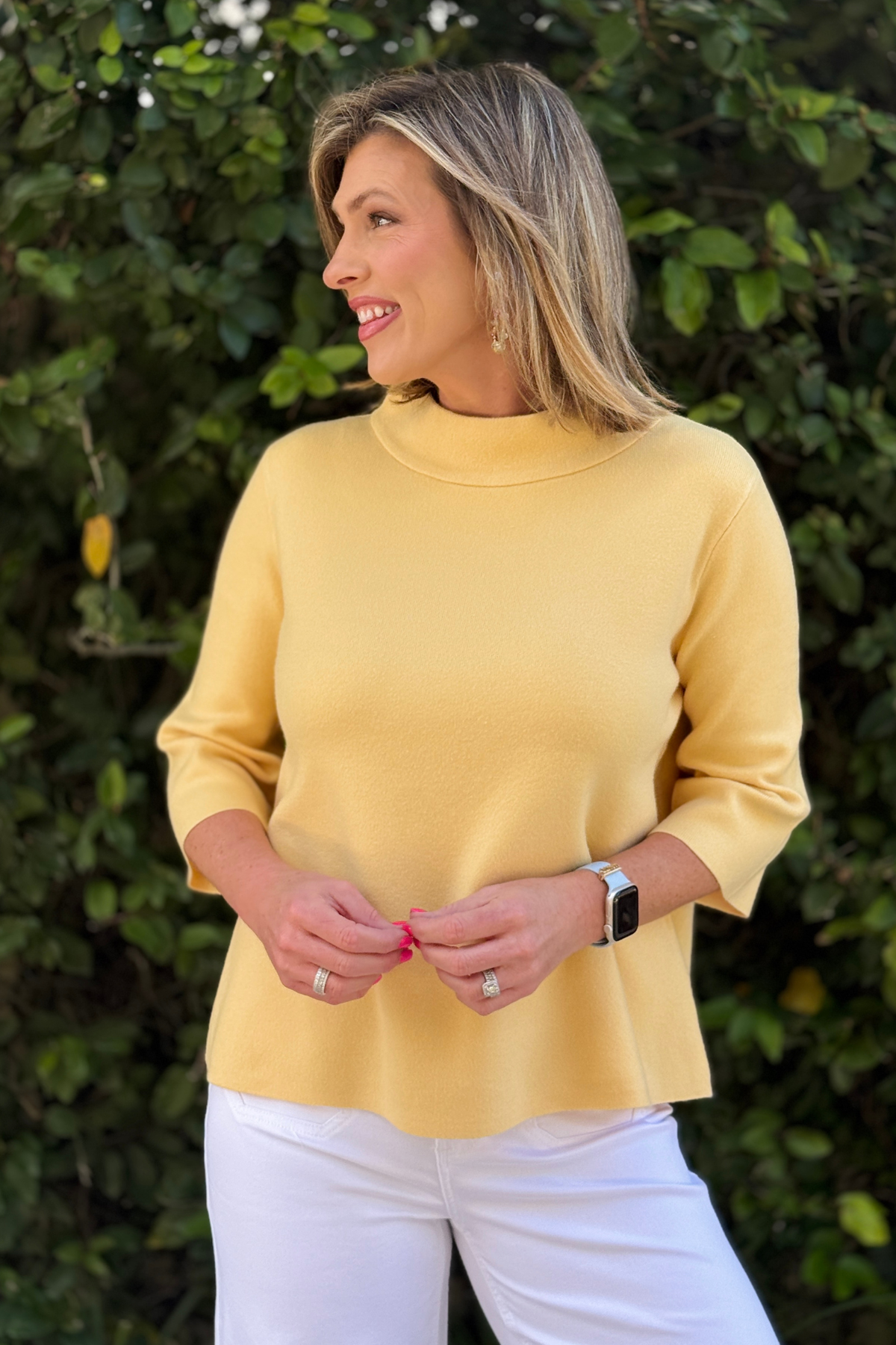 Woman wearing lightweight yellow mock neck bell sleeve sweater with white pants