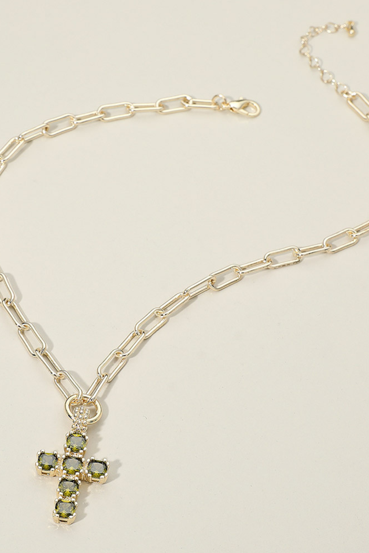 Gold paperclip chain necklace with a green CZ cluster cross pendant.