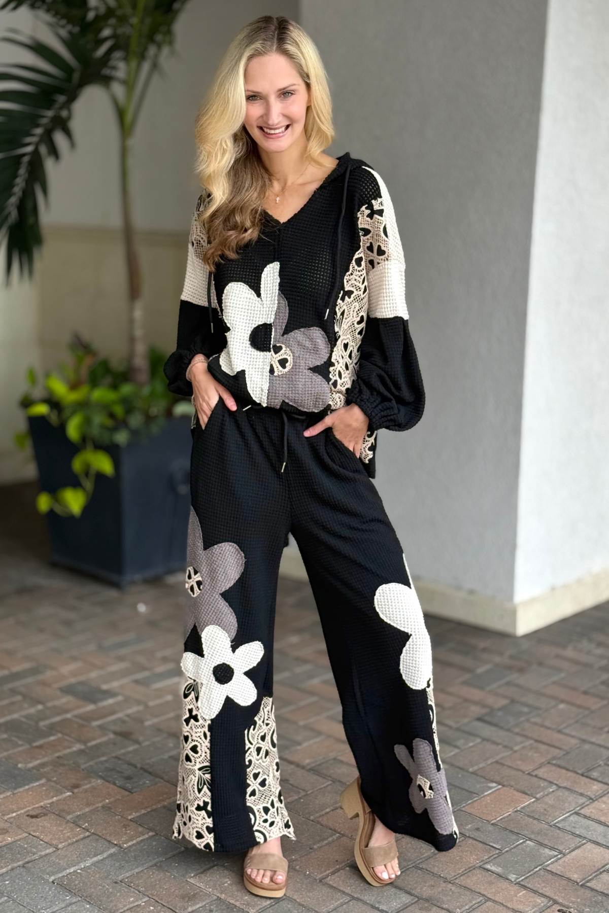 Model wearing black wide leg waffle knit pants with floral appliqués and crochet lace details.