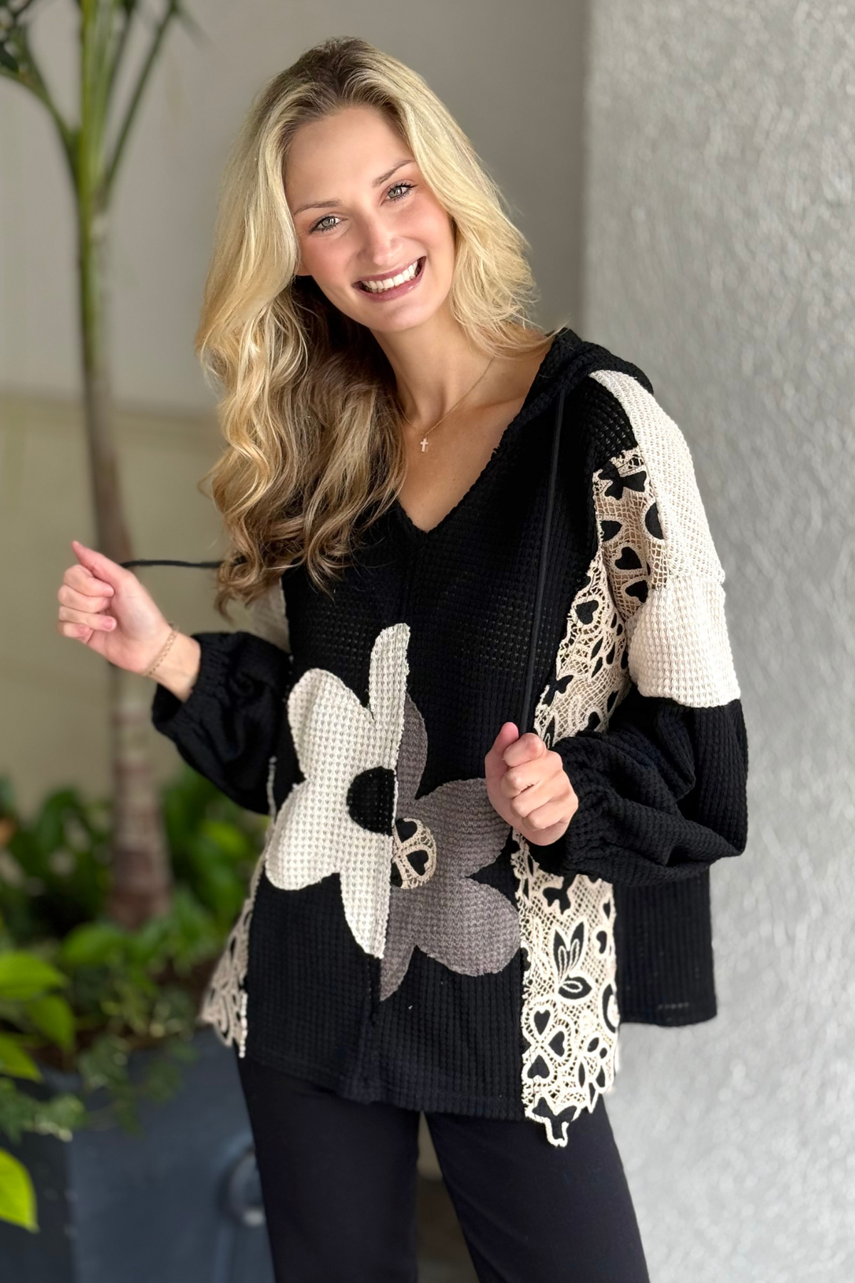 Model wearing black waffle knit hoodie with floral appliqués and crochet lace patches.