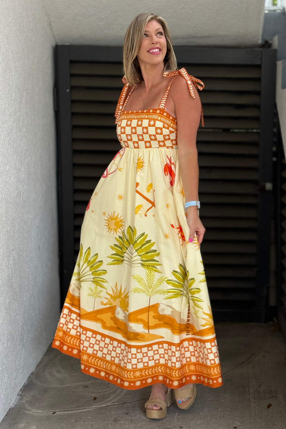 Woman wearing ivory tropical maxi dress with orange coastal print and tie straps