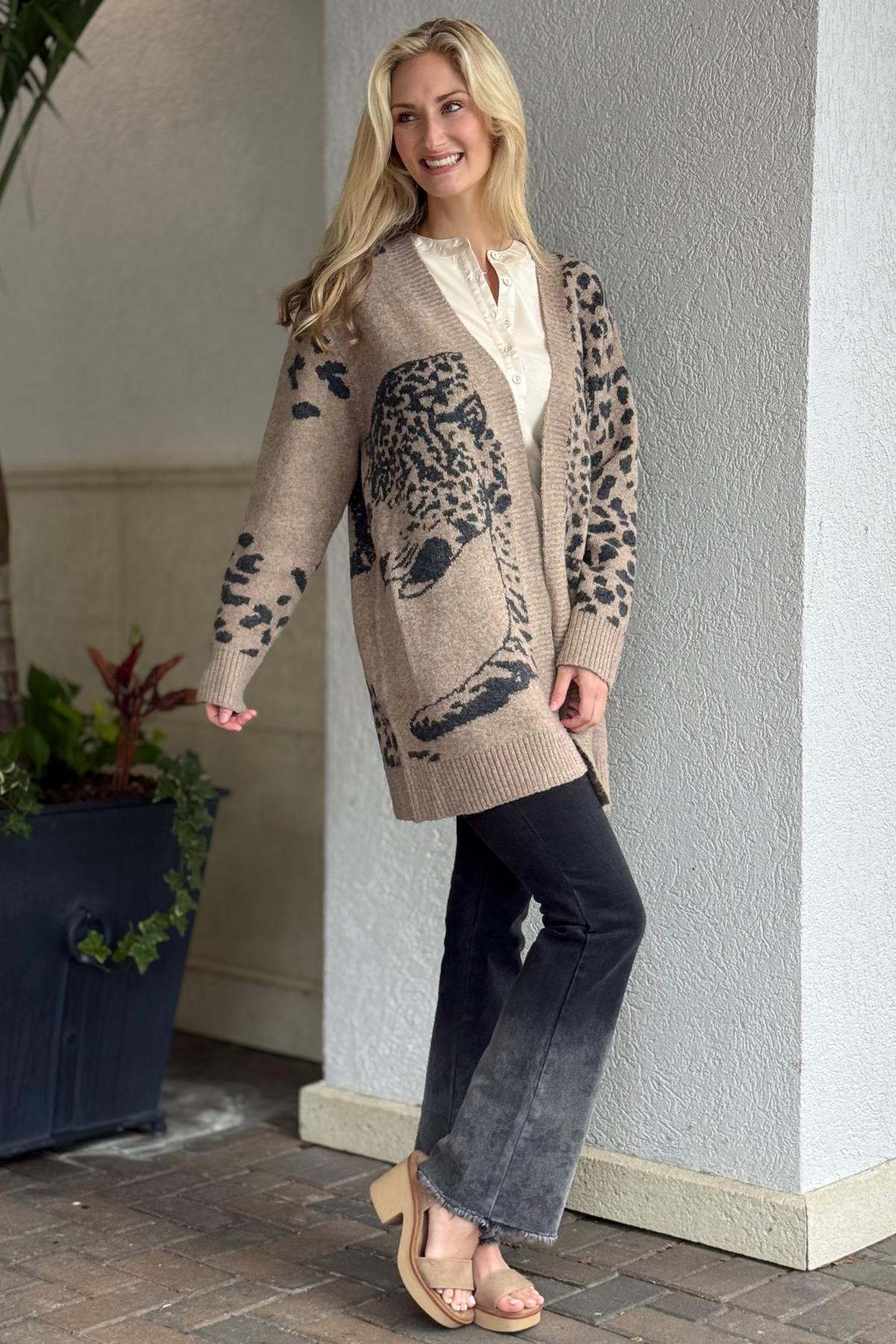 Model wearing The Duval Wildcat Cardigan — long tan knit cardigan with bold black animal jacquard design, open front, and front pockets.